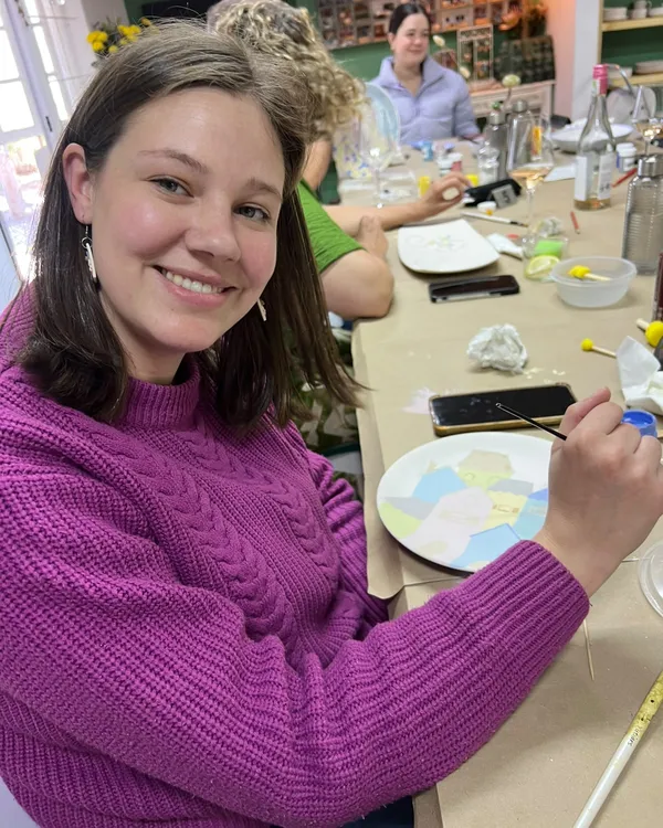 A customer in a purple jumper painting a plate of pastel houses