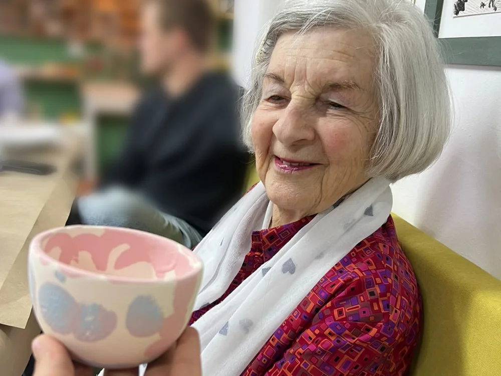 Ouma smiling at her painted pink and blue bowl, held up in front of her