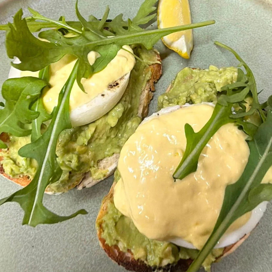 Avo Breakfast: sourdough toast with mashed avo, poached eggs, hollandaise and rocket on a sage green plate
