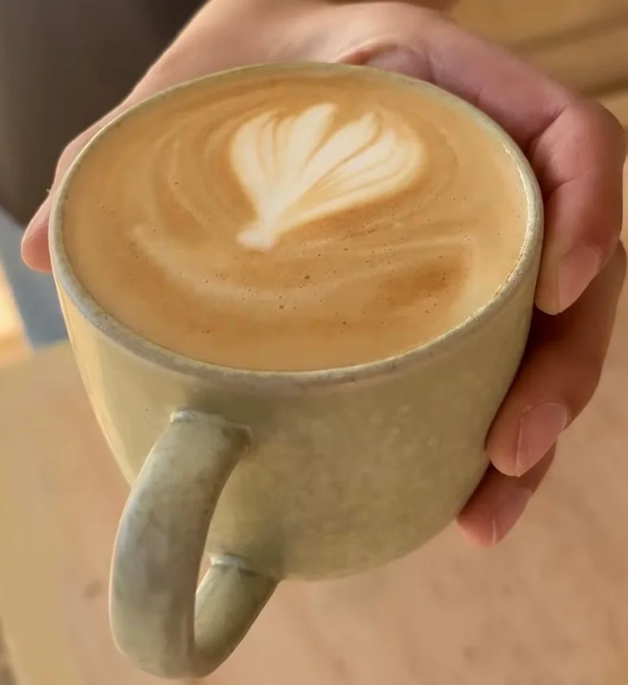 A flat white with latte art, held out in one of our sage green mugs