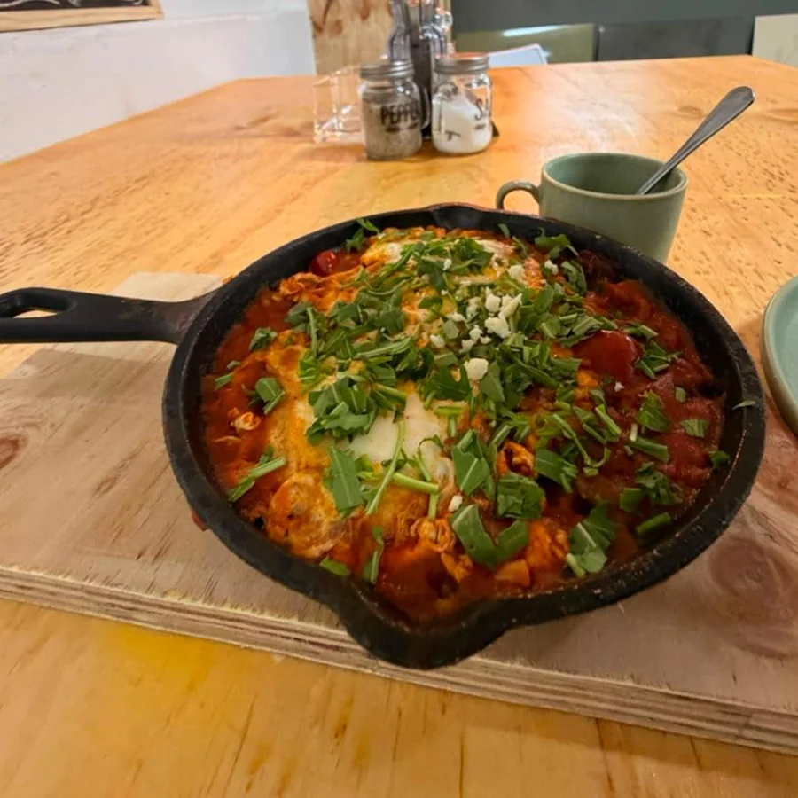 Shakshuka in a cast-iron pan, topped with fresh herbs and feta, on a wooden table in the cafe