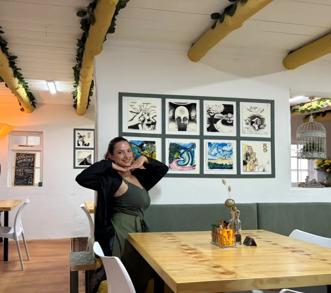Inside the Mustard Seed Cafe: leaf garlands on the mustard beams, Angie at a wooden table, Mike Wald paintings on the wall