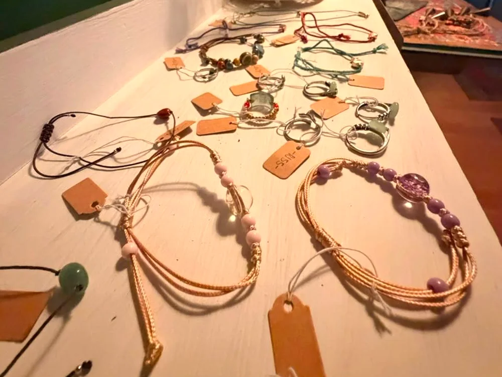 Bracelets, rings and necklaces with brown paper price tags on a white shelf in the cafe's little shop